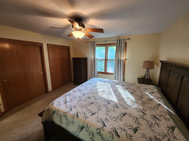 bedroom featuring ceiling fan, a textured ceiling, two closets, and carpet flooring