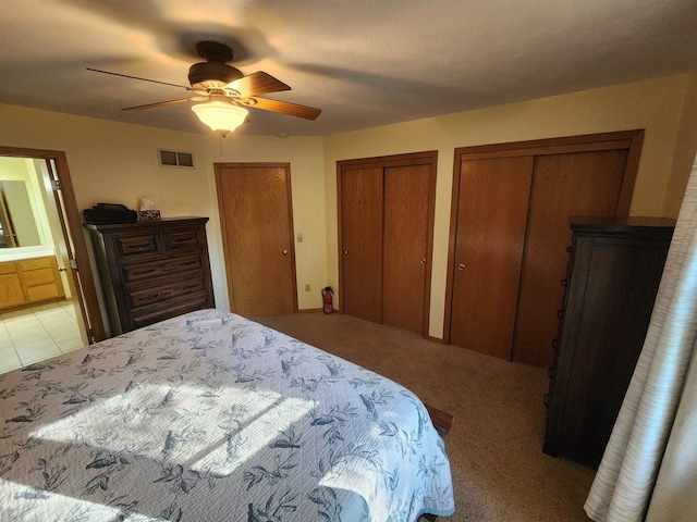 bedroom featuring connected bathroom, light carpet, ceiling fan, and multiple closets