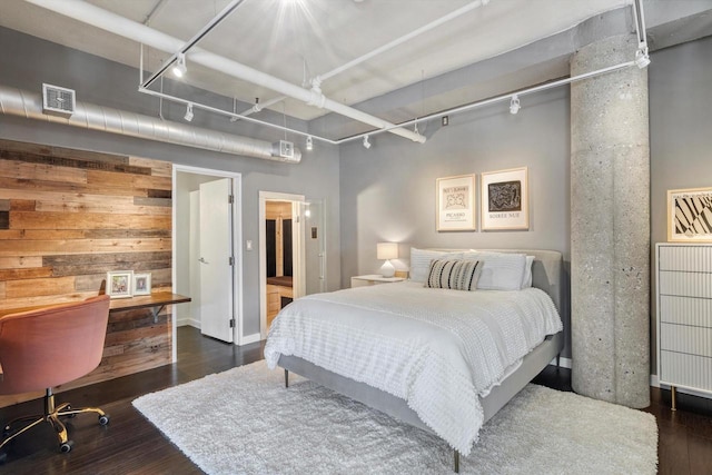 bedroom with wooden walls, rail lighting, and dark hardwood / wood-style flooring