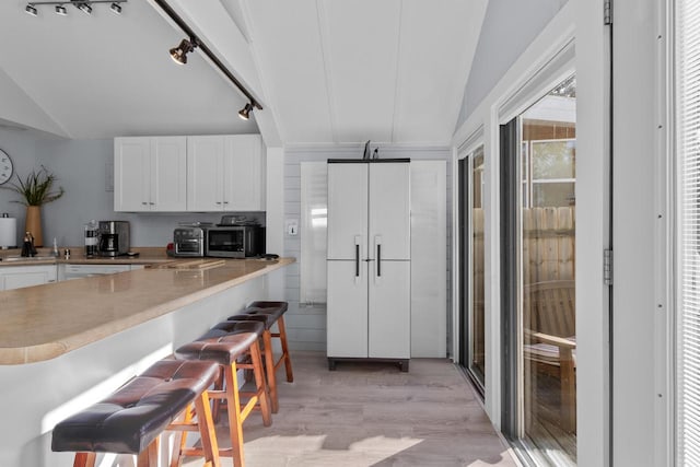 kitchen featuring a barn door, white cabinets, vaulted ceiling, and light hardwood / wood-style flooring