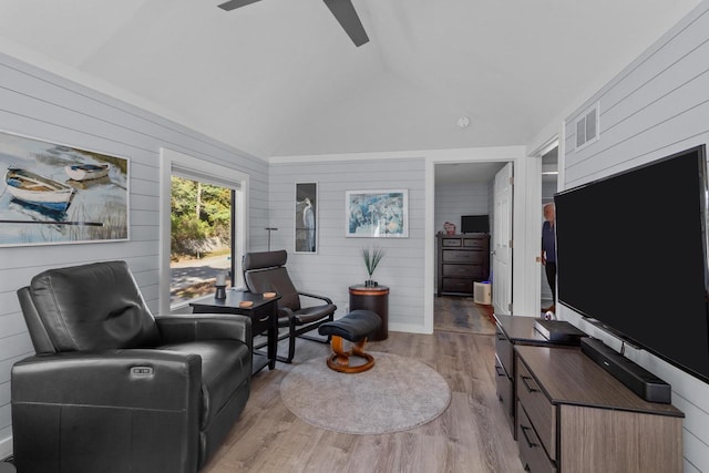 living room featuring high vaulted ceiling, wooden walls, and light hardwood / wood-style flooring