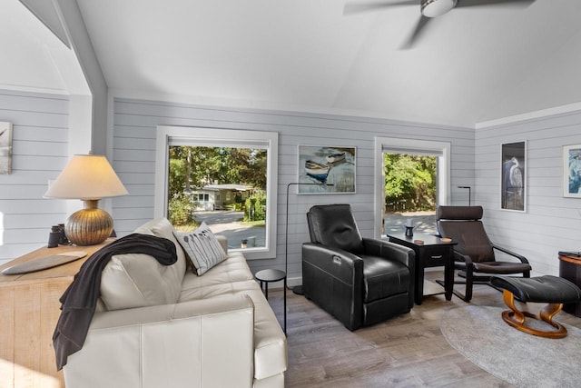 living room with lofted ceiling, wooden walls, light wood-type flooring, and a healthy amount of sunlight