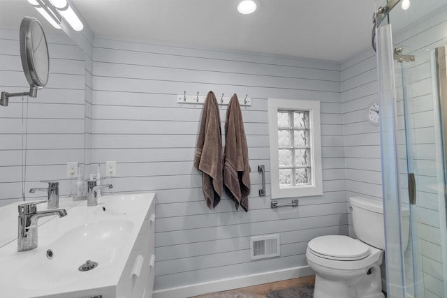 bathroom with an enclosed shower, vanity, wood walls, and toilet