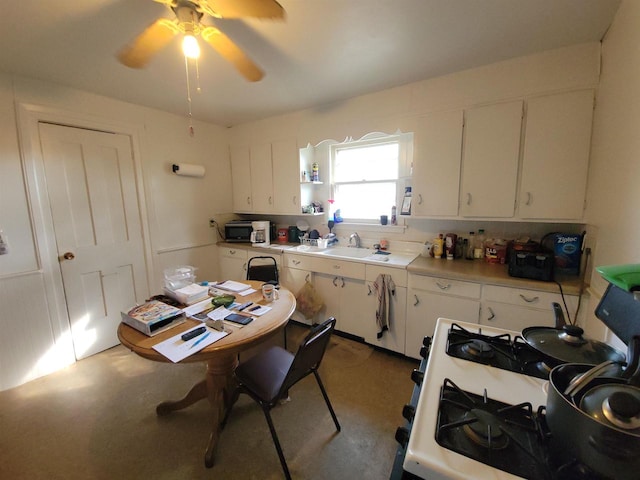 kitchen featuring white gas range, sink, ceiling fan, and white cabinets