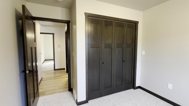 bedroom with a closet, light carpet, and baseboards