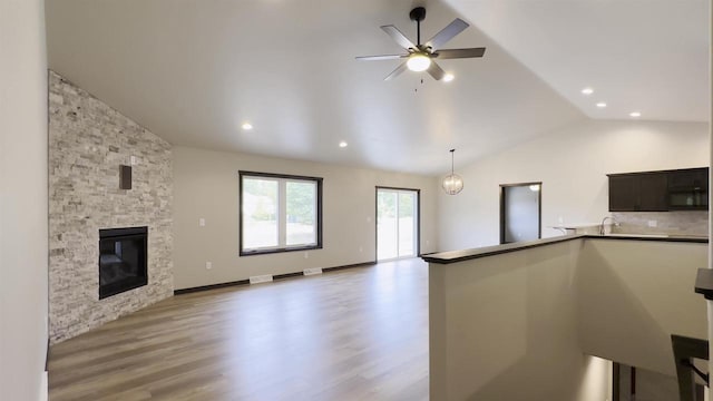 kitchen with open floor plan, a stone fireplace, black microwave, light wood finished floors, and vaulted ceiling