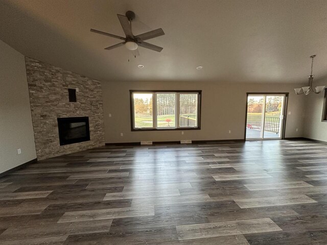 unfurnished living room with baseboards, vaulted ceiling, a stone fireplace, ceiling fan with notable chandelier, and dark wood-style flooring