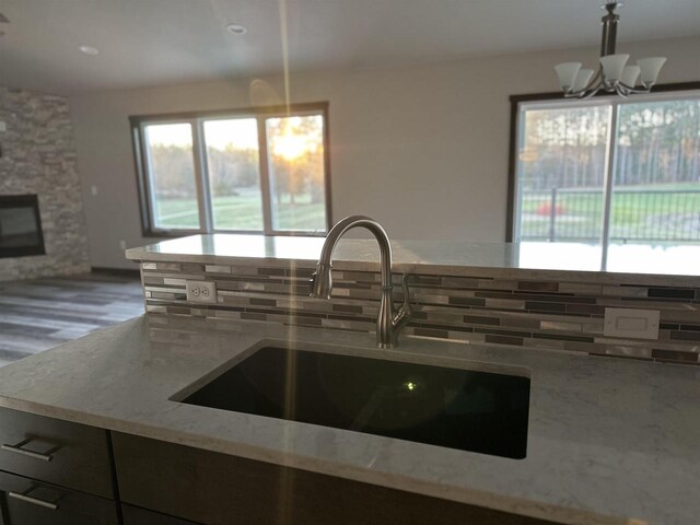 kitchen with a sink, a stone fireplace, an inviting chandelier, decorative backsplash, and light stone countertops