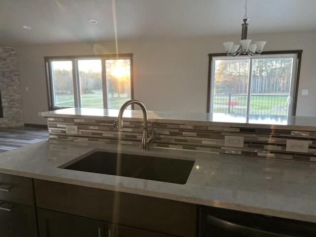 kitchen with a sink, decorative light fixtures, light stone counters, and stainless steel dishwasher