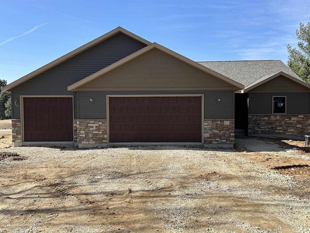 view of front of property featuring stone siding, an attached garage, and driveway