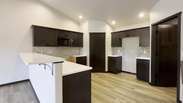 kitchen featuring a peninsula, light wood-style flooring, lofted ceiling, recessed lighting, and stainless steel microwave