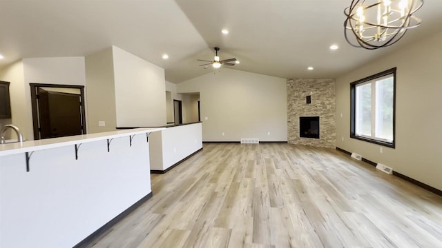 kitchen featuring visible vents, a kitchen bar, a stone fireplace, light countertops, and vaulted ceiling