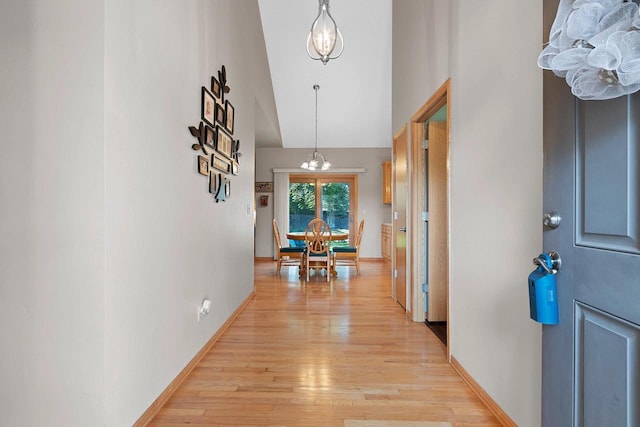 hall with high vaulted ceiling, light hardwood / wood-style flooring, and a notable chandelier