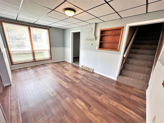 unfurnished room with built in shelves, a drop ceiling, and hardwood / wood-style flooring