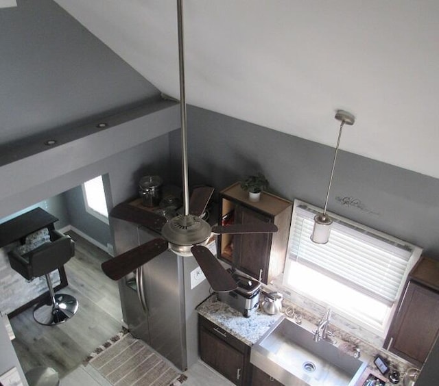 kitchen featuring dark brown cabinets, light wood-type flooring, lofted ceiling, and light stone countertops