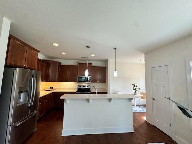 kitchen featuring an island with sink, appliances with stainless steel finishes, dark hardwood / wood-style floors, and decorative light fixtures