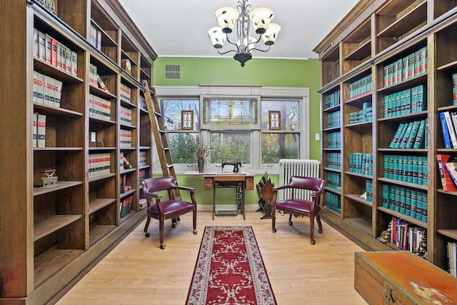 living area with a notable chandelier, light hardwood / wood-style flooring, and radiator heating unit