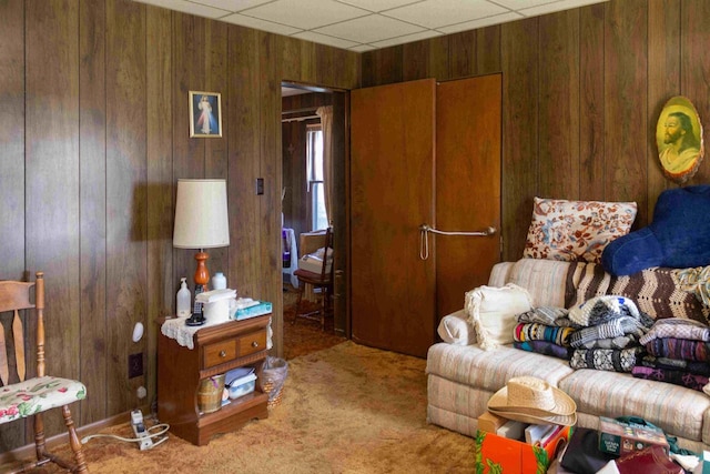 living room featuring a drop ceiling, wooden walls, and carpet floors