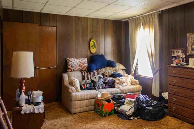 living room featuring a drop ceiling, wood walls, and carpet floors