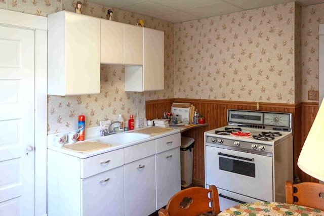 kitchen featuring white cabinets, wood walls, white range with gas cooktop, and sink