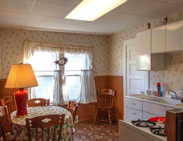 dining room with a paneled ceiling, wood walls, and sink