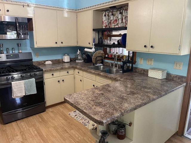 kitchen with sink, light hardwood / wood-style flooring, gas range oven, kitchen peninsula, and cream cabinetry