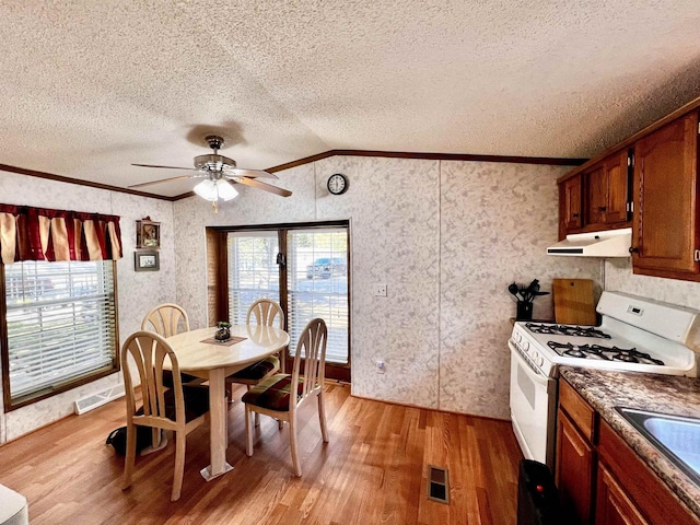 dining room featuring ceiling fan, ornamental molding, light wood-type flooring, and vaulted ceiling