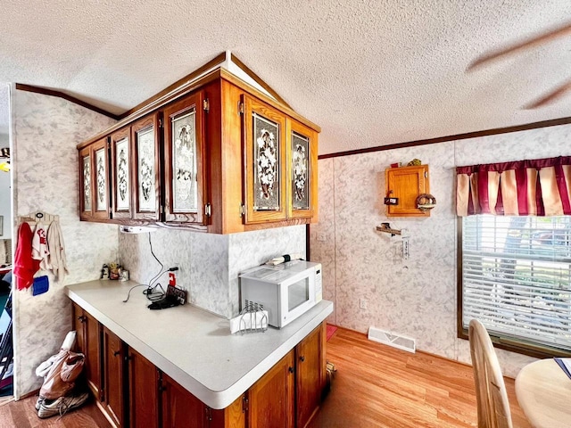 kitchen with a textured ceiling, light wood-type flooring, and ornamental molding