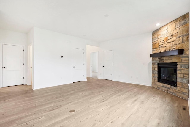 unfurnished living room with a stone fireplace and light wood-type flooring