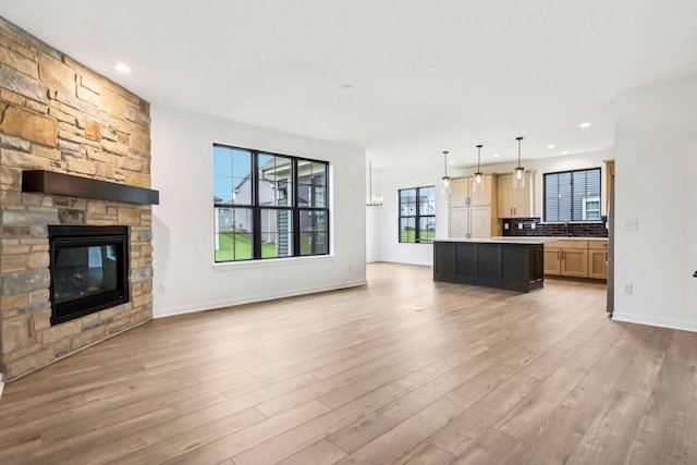 unfurnished living room with sink, light wood-type flooring, a fireplace, and a chandelier