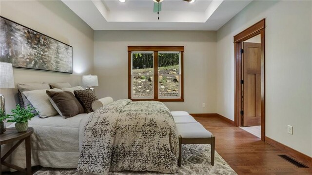 bedroom with ceiling fan, wood-type flooring, and a raised ceiling