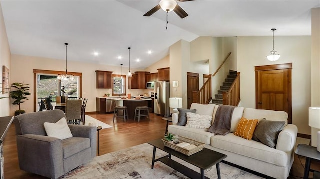 living room with ceiling fan with notable chandelier, dark wood-type flooring, and high vaulted ceiling