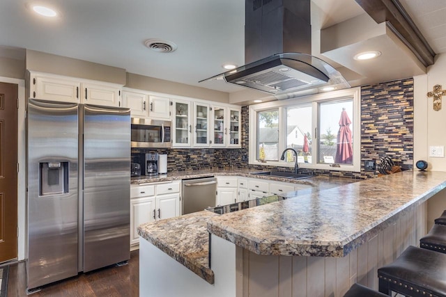 kitchen featuring appliances with stainless steel finishes, a kitchen breakfast bar, white cabinetry, island range hood, and kitchen peninsula