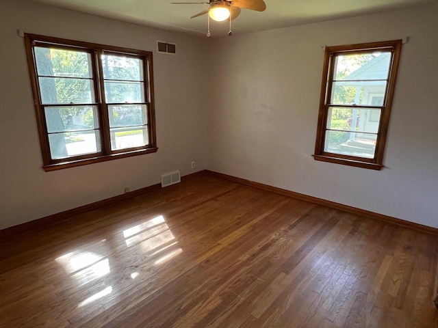 empty room with ceiling fan, a healthy amount of sunlight, and hardwood / wood-style floors