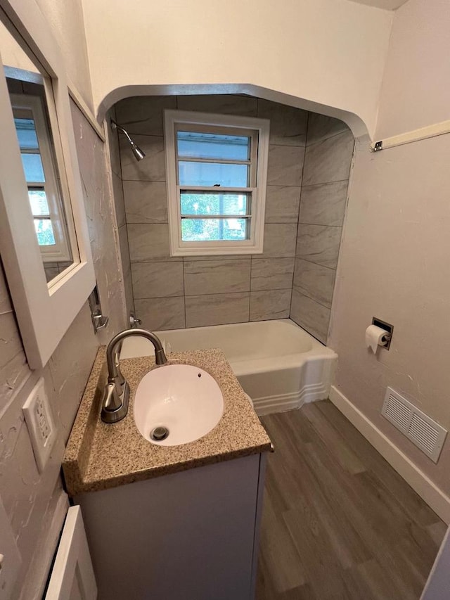 bathroom with hardwood / wood-style flooring, vanity, and tiled shower / bath