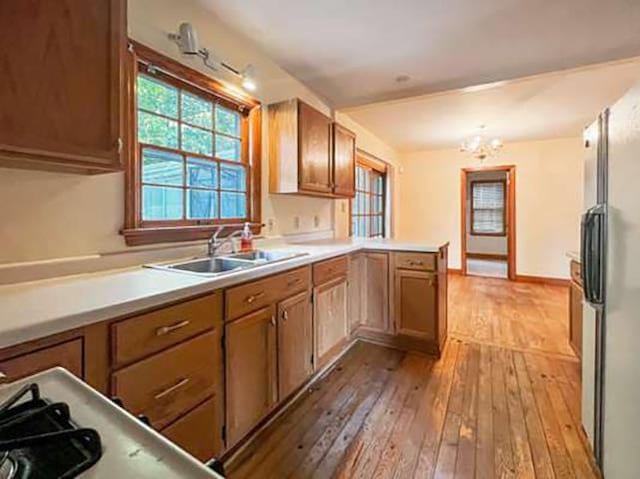 kitchen featuring light hardwood / wood-style floors, range, sink, an inviting chandelier, and stainless steel fridge