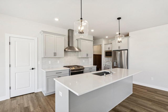 kitchen with pendant lighting, a center island with sink, wall chimney range hood, sink, and appliances with stainless steel finishes