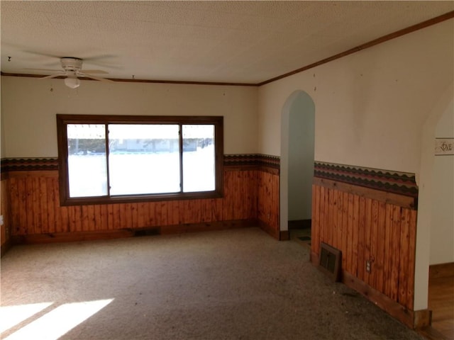 unfurnished room featuring light carpet, wood walls, a textured ceiling, and ceiling fan