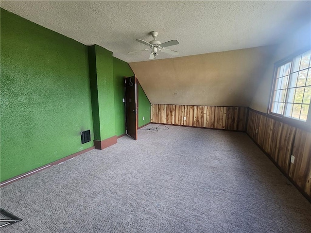 carpeted empty room featuring ceiling fan, a textured ceiling, wooden walls, and lofted ceiling