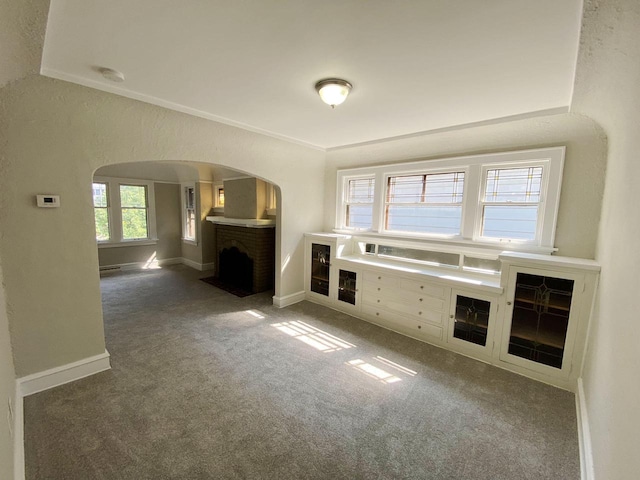 unfurnished living room featuring crown molding, dark carpet, and a brick fireplace