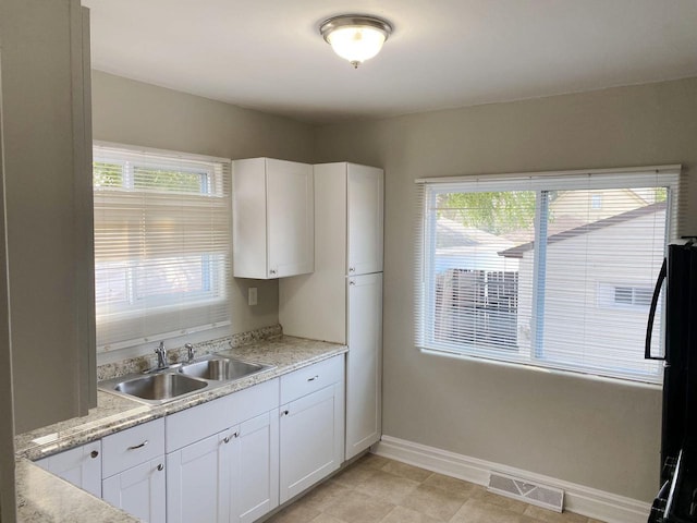 kitchen featuring light tile patterned floors, sink, white cabinetry, fridge, and light stone countertops