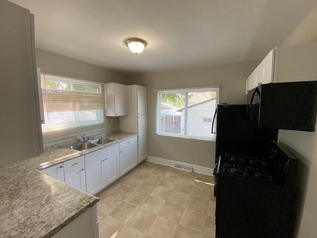 kitchen featuring black gas range, light stone counters, sink, and white cabinetry