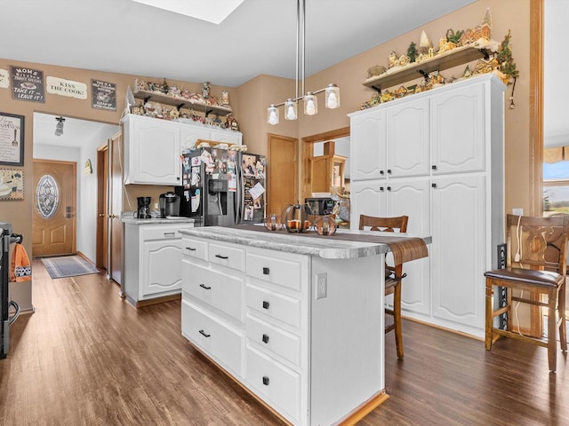 kitchen featuring hanging light fixtures, white cabinetry, dark wood-type flooring, a kitchen island, and black fridge