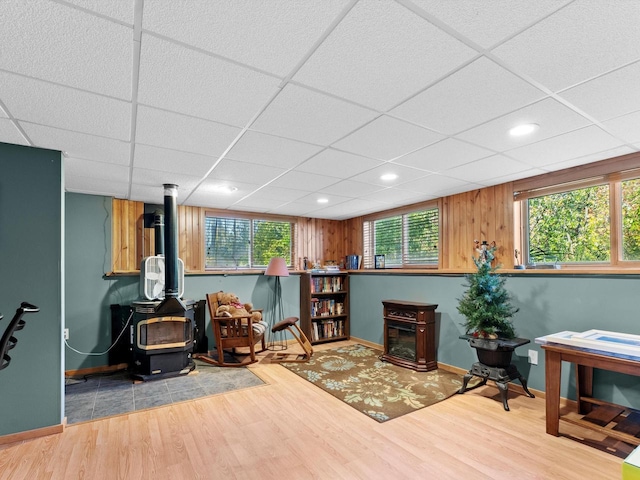 living area with a drop ceiling, a wood stove, a wealth of natural light, and hardwood / wood-style flooring