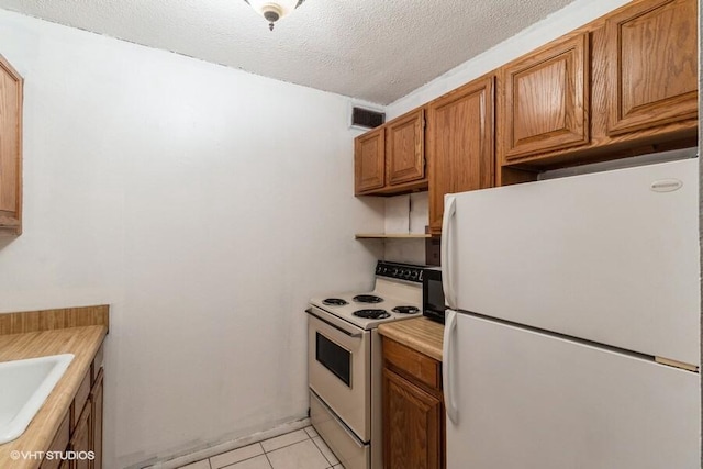 kitchen featuring white appliances, a textured ceiling, and light tile patterned flooring