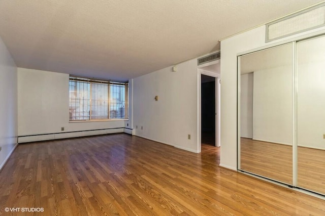 unfurnished bedroom featuring a closet, a baseboard heating unit, wood-type flooring, and a textured ceiling