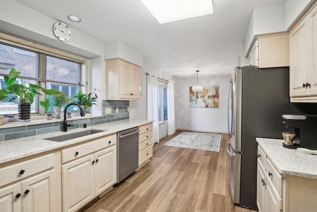 kitchen with light stone countertops, appliances with stainless steel finishes, sink, hanging light fixtures, and light hardwood / wood-style floors