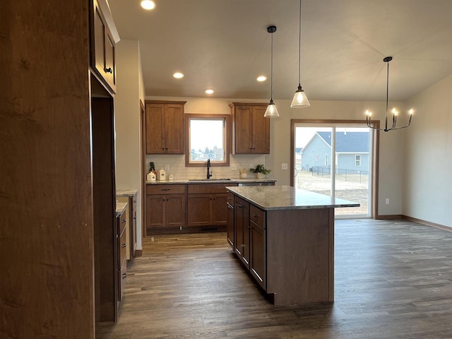 kitchen with light stone countertops, hanging light fixtures, sink, a kitchen island, and dark wood-type flooring