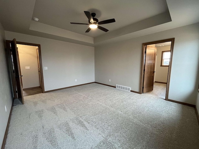 unfurnished bedroom featuring ceiling fan, a raised ceiling, and light carpet