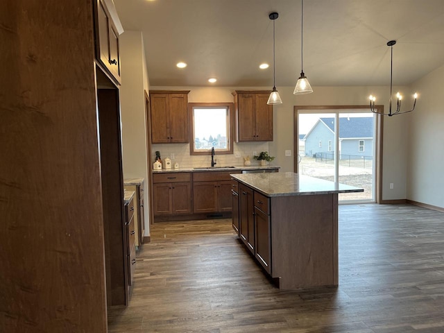 kitchen with a center island, sink, pendant lighting, dark wood-type flooring, and light stone counters